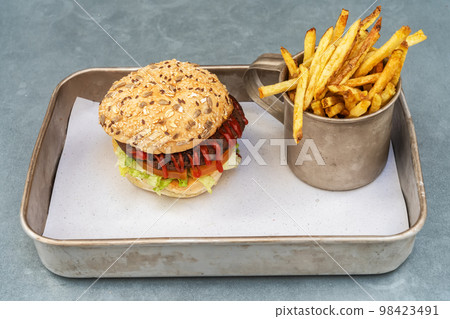 Vegetarian hamburger from beans vegetables and ketchup buns and fried potatoes in a vintage mug on a metal tray. Vegetarian hamburger from beans vegetables and ketchup buns and fried potatoes in a vintage mug on a metal tray. 98423491