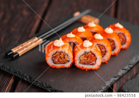 Sushi roll with tuna, onion in batter and tobiko caviar served on black board close-up - Japanese food Sushi roll with tuna, onion in batter and tobiko caviar served on black board close-up - Japanese food 98423558