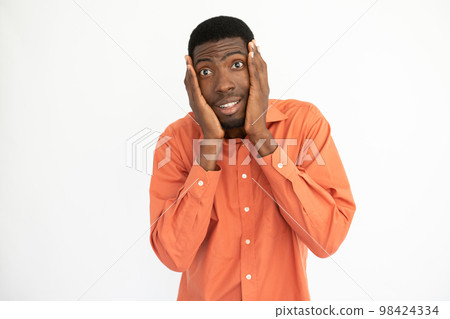 Portrait of amazed young man holding face in hands Portrait of amazed young man holding face in hands 98424334