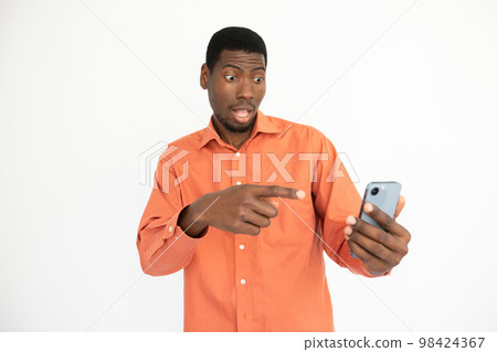 Portrait of surprised young man pointing at mobile phone Portrait of surprised young man pointing at mobile phone 98424367