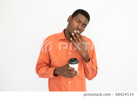 Portrait of tired young man holding coffee cup and yawning 98424514