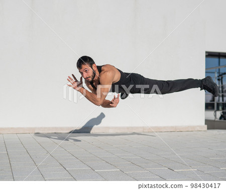 A man in black sportswear jumps while doing push-ups outdoors. A man in black sportswear jumps while doing push-ups outdoors. 98430417