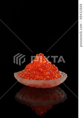 Red caviar in a transparent dish in the form of a shell on a black background. Vertical photo. 98432889