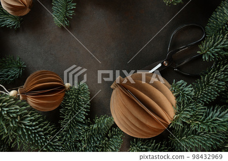 Christmas toys in shape of ball made of craft paper.Scissors for cutting out paper.Handmade work.Craft paper.Spruce branches.Flat lying.Space for text.Greeting card for holiday.New Year or Christmas. 98432969