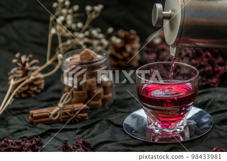 Roselle tea (Jamaica sorrel, Rozelle or hibiscus sabdariffa ) is poured from a kettle into glass cup with dry roselle and brown cane sugar cube. Roselle tea (Jamaica sorrel, Rozelle or hibiscus sabdariffa ) is poured from a kettle into glass cup with dry roselle and brown cane sugar cube. 98433981