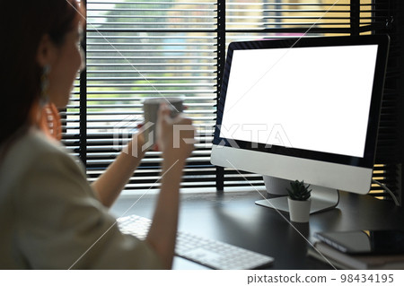 Computer monitor view over female shoulder, businesswoman holding coffee cup and reading email on computer 98434195