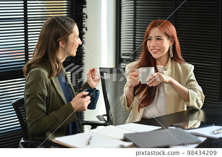 Attractive asian businesswoman drinking coffee while having conversation with her business partner in modern office Attractive asian businesswoman drinking coffee while having conversation with her business partner in modern office 98434209