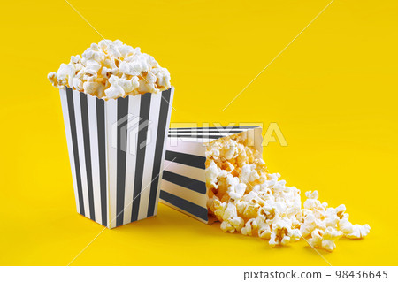 Two black white striped carton buckets with tasty cheese popcorn, isolated on yellow background Two black white striped carton buckets with tasty cheese popcorn, isolated on yellow background 98436645