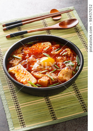 Sundubu jjigae is a Korean stew made with soft tofu, kimchi, pork belly, onion and spices closeup on the bowl. Vertical Sundubu jjigae is a Korean stew made with soft tofu, kimchi, pork belly, onion and spices closeup on the bowl. Vertical 98437052