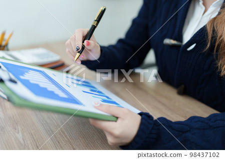 Portrait of a thoughtful Asian businesswoman looking at financial statements and making marketing plans using a computer on her desk. 98437102