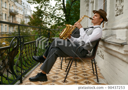 Handsome jazzman enjoys playing saxophone relaxing on terrace Handsome jazzman enjoys playing saxophone relaxing on terrace 98437253