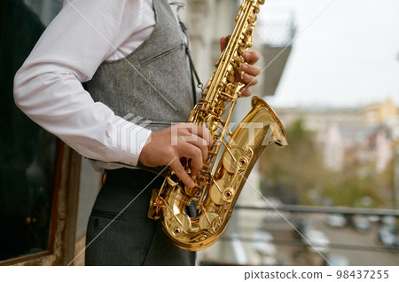 Saxophonist playing music outdoors, closeup saxophone in musician hand Saxophonist playing music outdoors, closeup saxophone in musician hand 98437255