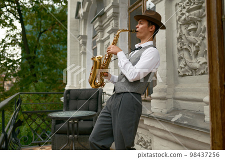 Young male musician practicing saxophone in balcony at home Young male musician practicing saxophone in balcony at home 98437256