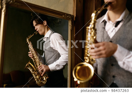Young man playing saxophone in reflection of mirror at home Young man playing saxophone in reflection of mirror at home 98437263