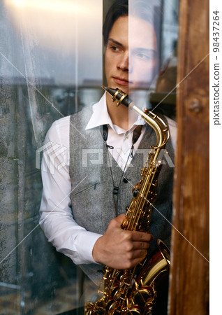 Young man saxophonist with instrument view from window Young man saxophonist with instrument view from window 98437264