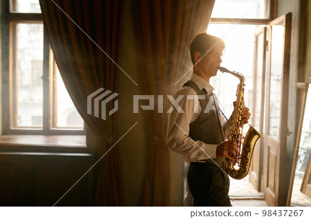 Young elegant man playing gold alto saxophone in misty room Young elegant man playing gold alto saxophone in misty room 98437267