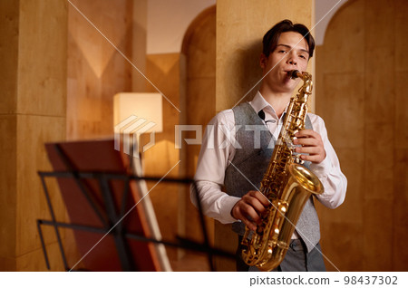 Jazz musician playing saxophone and leaning against art studio wall Jazz musician playing saxophone and leaning against art studio wall 98437302