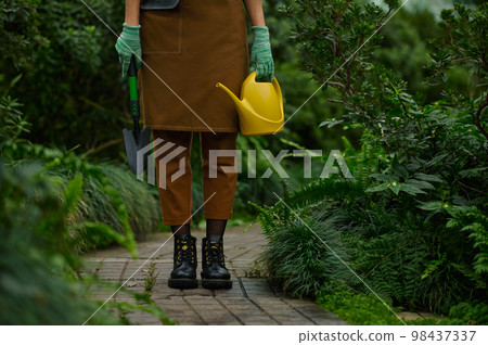 Cropped shot of gardener holding garden tool view on leg Cropped shot of gardener holding garden tool view on leg 98437337