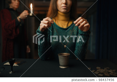 Woman making divination with ring under mature professional gypsy control Woman making divination with ring under mature professional gypsy control 98437456