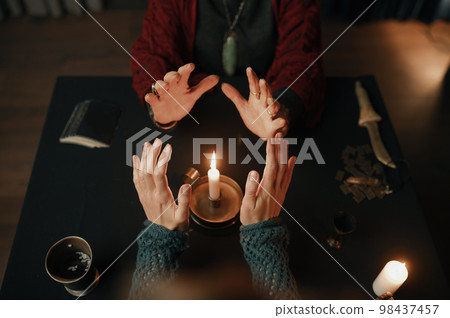 Clairvoyant and client holding hand over candle flame top view Clairvoyant and client holding hand over candle flame top view 98437457