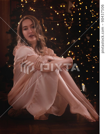 Young girl in a transparent tunic with sitting on the background of the Christmas tree. 98437506