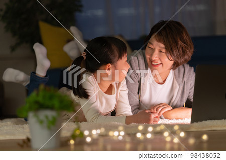 Elementary school girl and mom lying in the living room at night and looking at a computer 98438052
