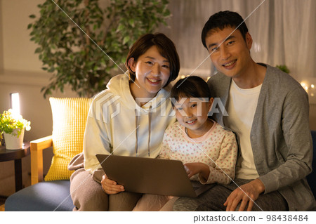 爸爸、媽媽和一個小學生晚上並排坐在沙發上看筆記本電腦 98438484