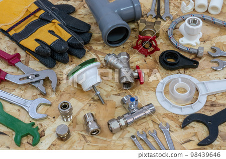 Plumbing tools, parts, pipeline components and gloves on the background of a construction OSB plate. Plumbing tools, parts, pipeline components and gloves on the background of a construction OSB plate. 98439646
