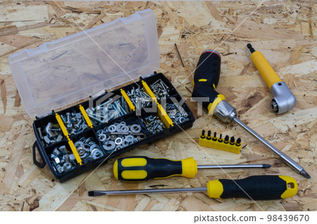 Case organizer with fasteners, a screwdrivers and a holder with bits on a osb construction plate background. Case organizer with fasteners, a screwdrivers and a holder with bits on a osb construction plate background. 98439670