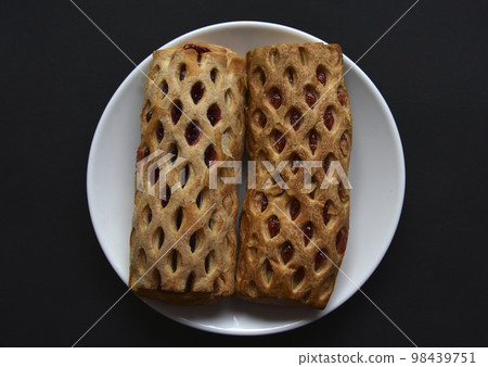 Sweet bun with jam on a white plate. Delicious bun with jam on a black background. 98439751