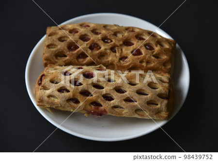 Sweet bun with jam on a white plate. Delicious bun with jam on a black background. 98439752