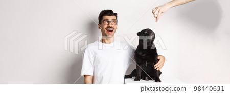 Amazed young man in glasses hugging his dog, pet owner and pug staring at upper left corner promo offer, standing over white background 98440631