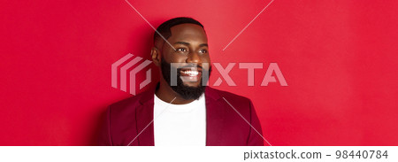 Close-up of handsome african american man with beard, looking left and smiling joyful, standing over red background 98440784