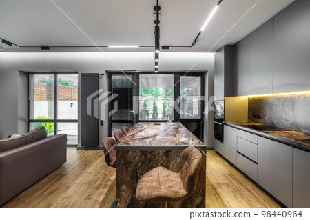 Modern luxury apartment with a free layout in a loft style in gray and dark colors. Stylish kitchen area with an island, marble countertop 98440964
