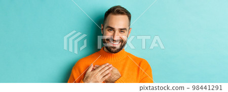 Close-up of handsome young man saying thank you, holding hands on heart and smiling grateful, standing over light blue background Close-up of handsome young man saying thank you, holding hands on heart and smiling grateful, standing over light blue background 98441291