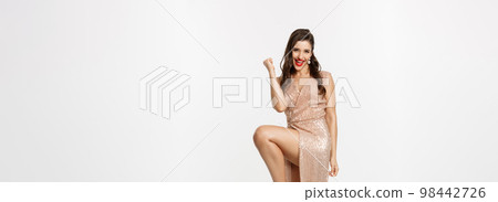Christmas party and celebration concept. Full length of lucky woman feeling excited, wearing elegant dress, making fist pump and rejoicing, winning Christmas party and celebration concept. Full length of lucky woman feeling excited, wearing elegant dress, making fist pump and rejoicing, winning 98442726