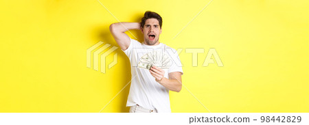Frustrated man holding money, shouting and panicking, standing over yellow background Frustrated man holding money, shouting and panicking, standing over yellow background 98442829