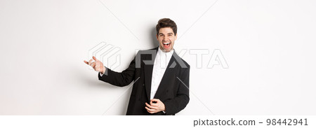 Portrait of happy man dancing at party, playing on invisible guitar and laughing, standing in black suit against white background Portrait of happy man dancing at party, playing on invisible guitar and laughing, standing in black suit against white background 98442941