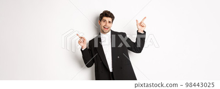 Handsome guy dancing and partying in black suit, pointing fingers sideways, showing two promo banners, standing against white background 98443025