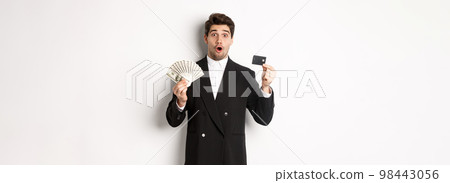 Portrait of surprised handsome man i suit, showing credit card with money, standing against white background Portrait of surprised handsome man i suit, showing credit card with money, standing against white background 98443056