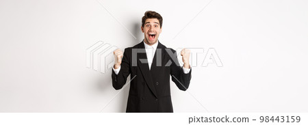 Image of happy and relieved businessman feeling lucky, making fist pumps and smiling with joy, achieve goal, winning and triumphing, standing over white background Image of happy and relieved businessman feeling lucky, making fist pumps and smiling with joy, achieve goal, winning and triumphing, standing over white background 98443159