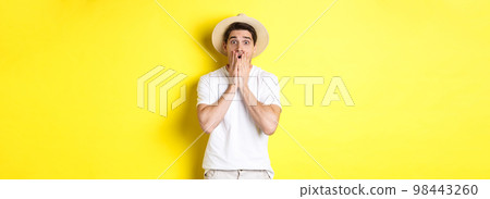 Concept of tourism and summer. Shocked guy jumping from fear, standing startled against yellow background Concept of tourism and summer. Shocked guy jumping from fear, standing startled against yellow background 98443260