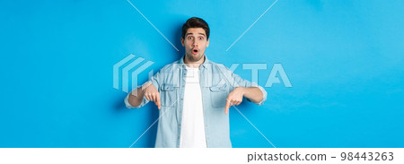 Surprised bearded adult man in casual outfit, pointing fingers down and looking startled, asking question about promotion, standing over blue background Surprised bearded adult man in casual outfit, pointing fingers down and looking startled, asking question about promotion, standing over blue background 98443263