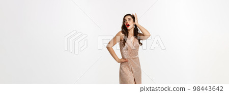 Party and celebration concept. Full-length of perfect woman in elegant dress laughing, standing near Christmas presents, white background 98443642