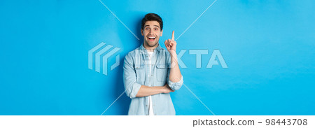 Image of handsome adult man having an idea, raising finger and smiling excited, found solution, standing against blue background Image of handsome adult man having an idea, raising finger and smiling excited, found solution, standing against blue background 98443708
