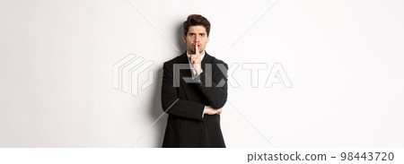 Portrait of angry boss in suit shushing at you, telling to be quiet, showing taboo hush sign and frowning, standing over white background 98443720
