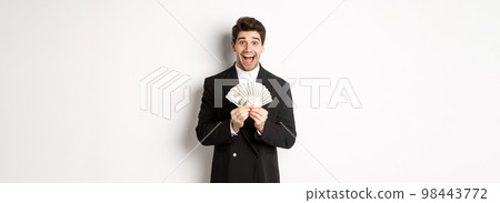 Portrait of handsome successful businessman in trendy suit, showing money and smiling amazed, earn cash, standing over white background 98443772