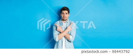 Portrait of nervous guy pointing fingers sideways, looking indecisive and asking for help with choice, showing left and right promo offers, standing against blue background Portrait of nervous guy pointing fingers sideways, looking indecisive and asking for help with choice, showing left and right promo offers, standing against blue background 98443792