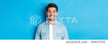 Close-up of smiling excited man with beard, looking amused at advertisement, standing against blue background 98443795