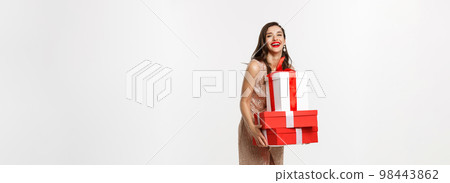 Party and celebration concept. Full-length of attractive brunette in glamour dress, holding Christmas gifts and laughing happy, white background Party and celebration concept. Full-length of attractive brunette in glamour dress, holding Christmas gifts and laughing happy, white background 98443862